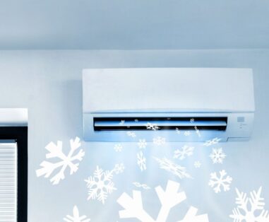 Wall-mounted air conditioner with white snowflake decorations on light blue wall, suggesting cooling in winter.