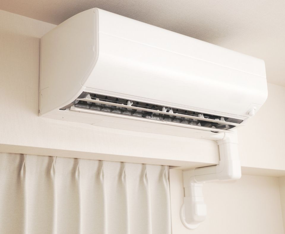 Wall-mounted white air conditioner unit above a beige curtain, with vents open.