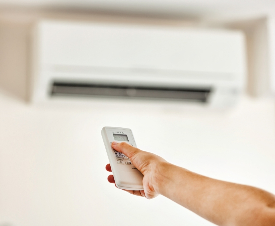 Hand holding a white remote control pointed at a wall-mounted air conditioner.